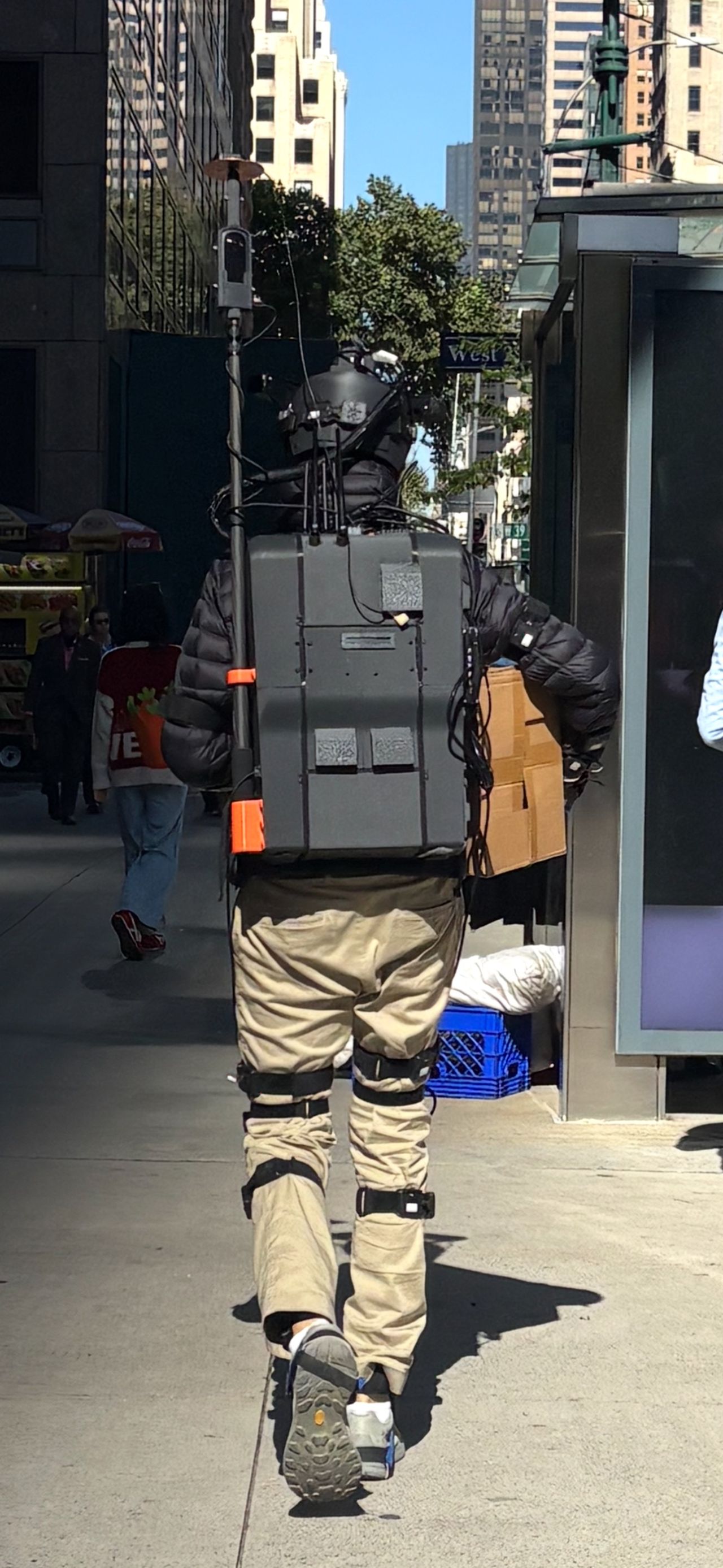 Operator wearing the THX rig and leg sensors, seen from behind on a sunny Midtown sidewalk